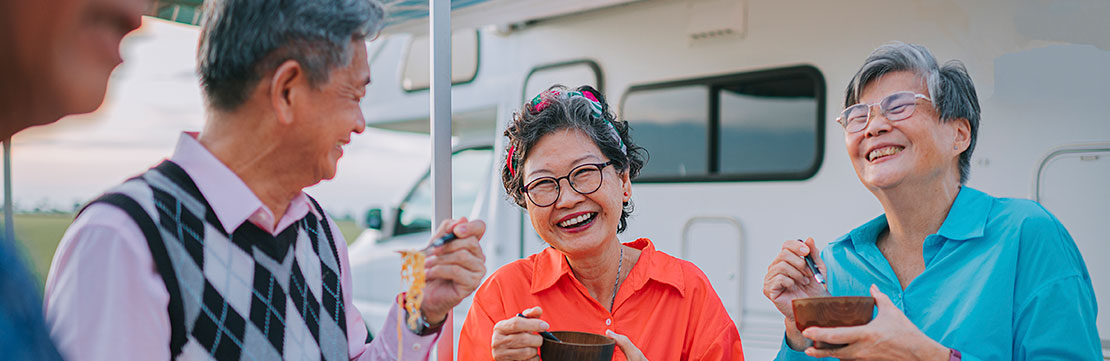 Group of seniors enjoy a meal together while standing beside a camper